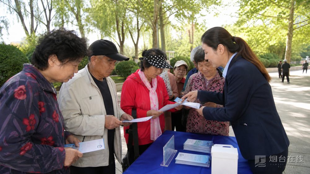 活动现场设有宣传展板和横幅,工作人员发放折页,并回答市民提问